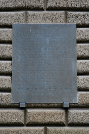 Lapide commemorativa che denuncia un'ingiustizia, visibile su una parete.