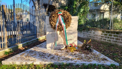 Monumento commemorativo con corona di fiori, dedica alle vittime dei bombardamenti, in un ambiente tranquillo e curato.
