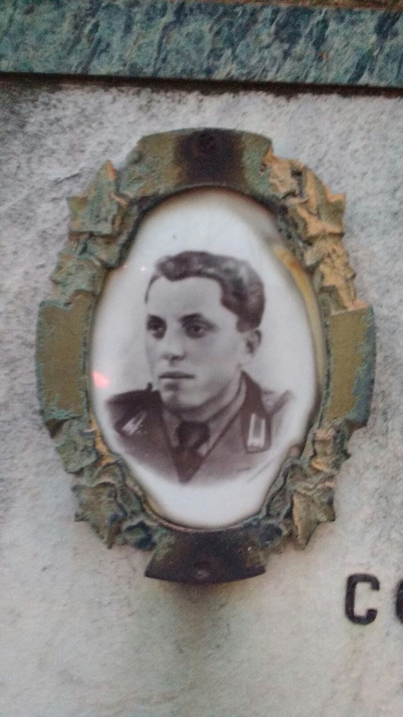 Ritratto ovale in ceramica di un giovane in uniforme, incorniciato in metallo su lapide di marmo.