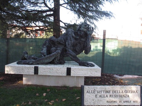 Monumento bronzeo che commemora le vittime della guerra e della Resistenza, immerso in verde.