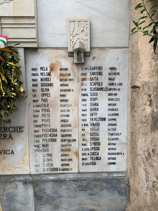 Monumento ai Caduti di Alghero, con incisioni commemorative e decorazioni floreali.
