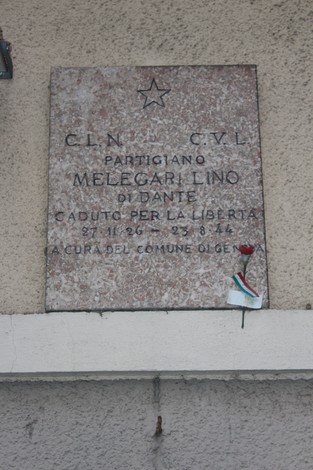 Lapide commemorativa in onore del partigiano Melegari Lino, caduto per la libertà. Decorata con un fiore e una bandiera.