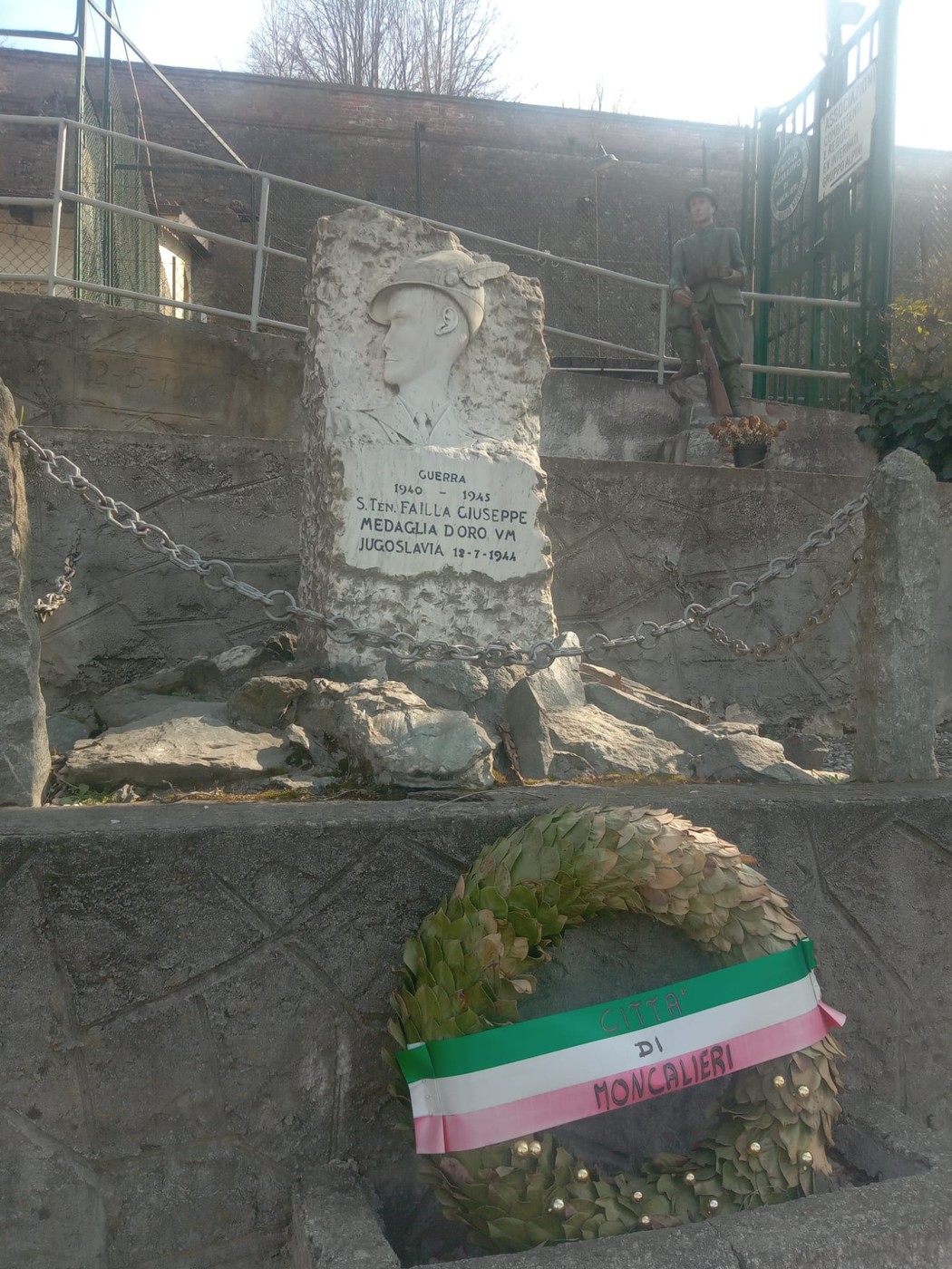 Cippo commemorativo dedicato a Giuseppe Failla, circondato da una corona di fiori e un ambiente tranquillo.