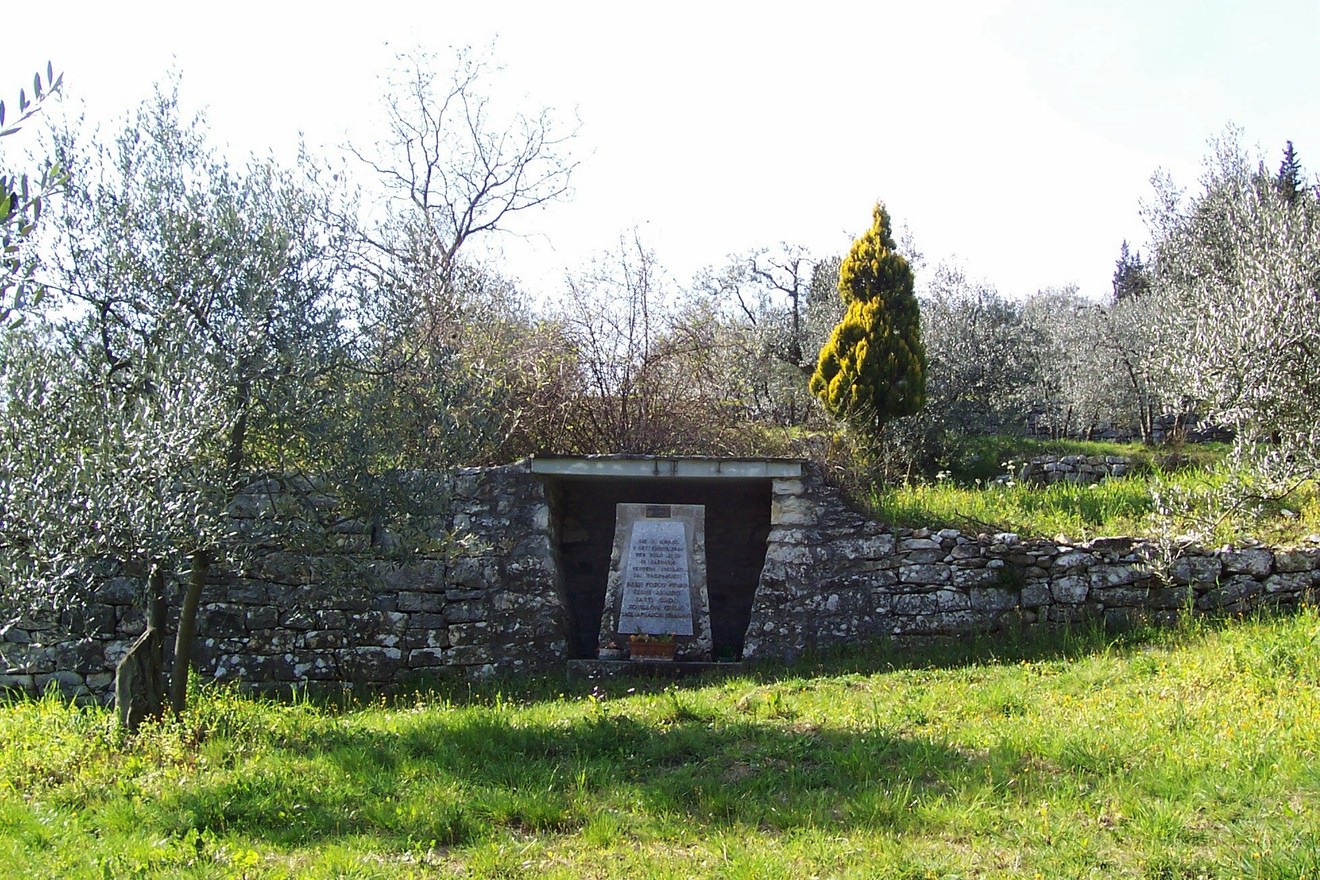 Cippo commemorativo immerso nella natura, dedicato ai caduti di Sommaia, circondato da uliveti e vegetazione.