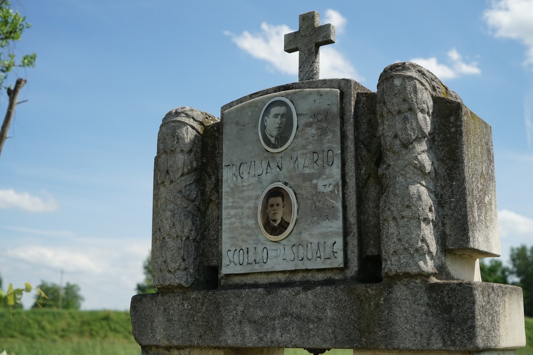 Cippo commemorativo con fotografie, dedicato a Scollo e Trevisan, in un contesto rurale sereno.
