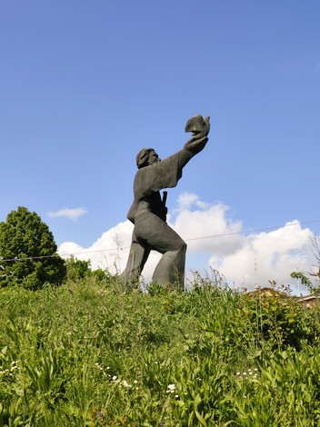Monumento al Partigiano, statua bronzea che raffigura un combattente che alza un elmetto, circondato da vegetazione.