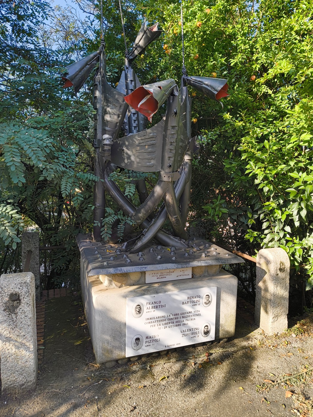 Monumento in memoria di Bartolini, Pizzoli, Zuppiroli e Albertini, circondato da vegetazione.