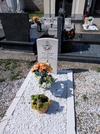 Tomba di Allan con fiori e decorazioni, situata in un cimitero, circondata da altre sepolture.