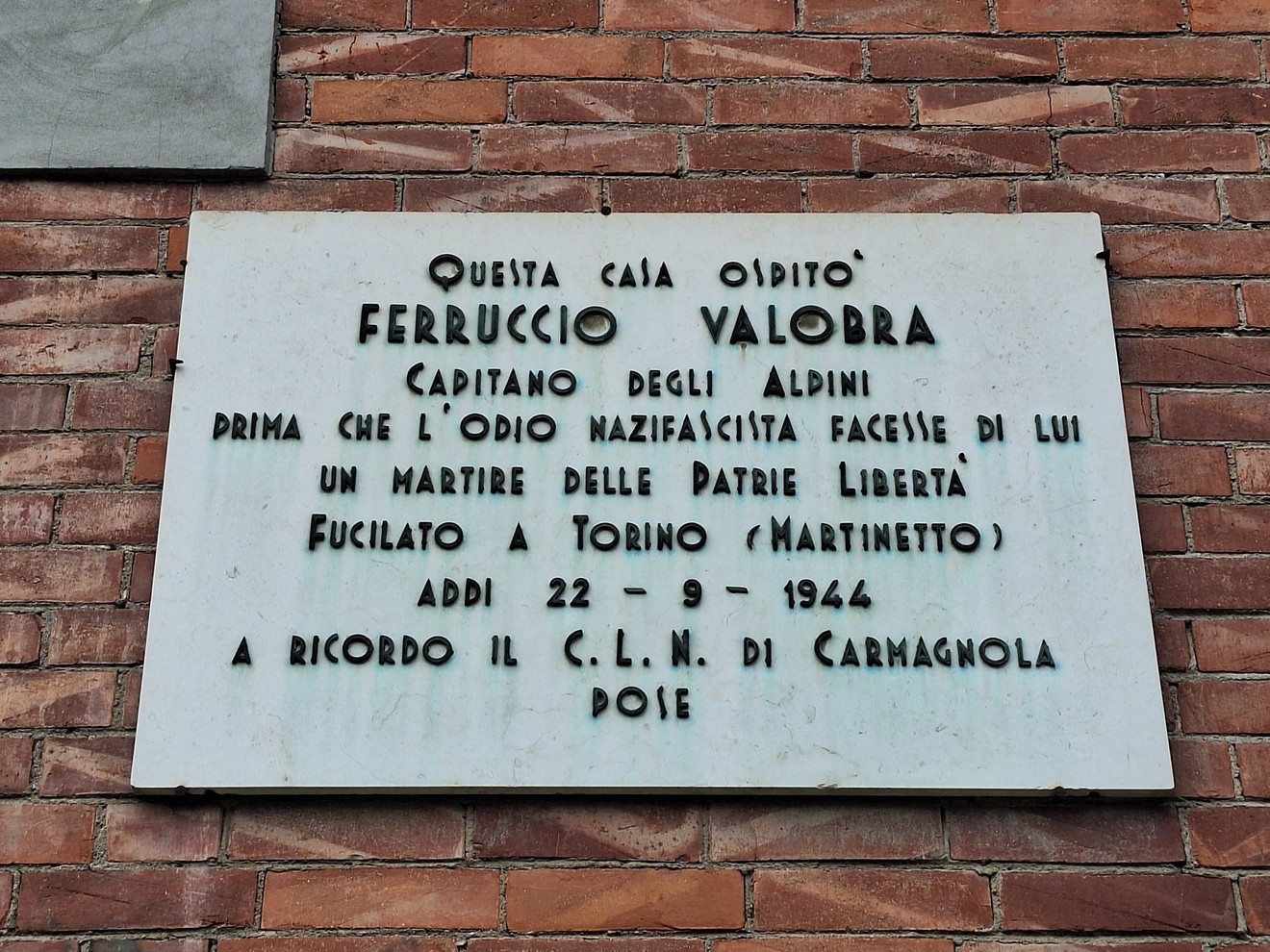 Lapide bianca con iscrizione dedicata a Ferruccio Valobra, affissa su una parete in mattoni a vista.