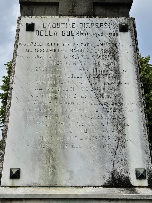 Monumento ai Caduti, con iscrizioni commemorative su una stele di marmo, immerso nel verde circostante.