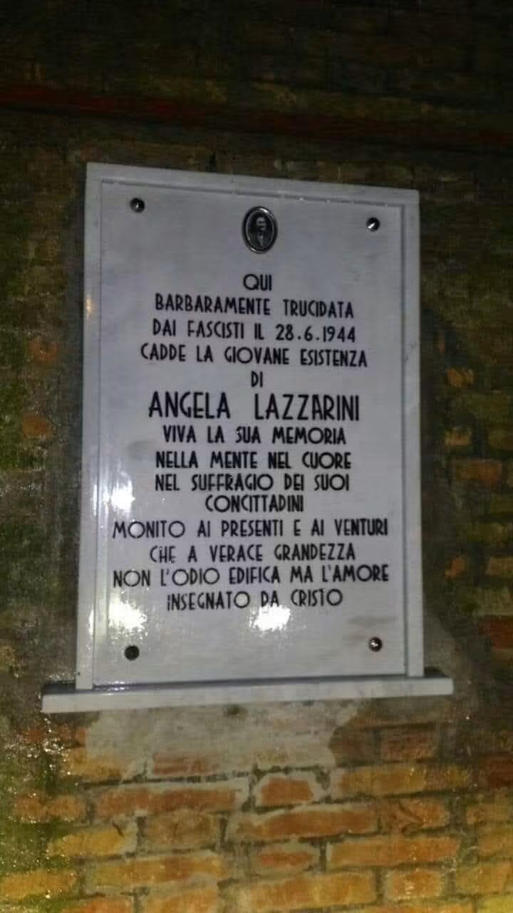 Lapide in marmo con iscrizione, fissata su una parete di mattoni a vista.