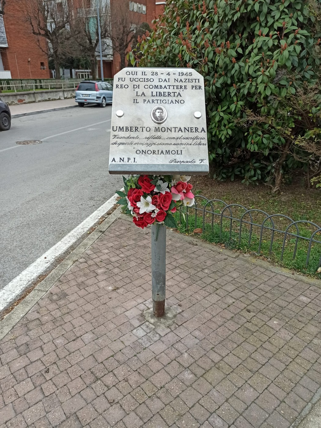 Lapide dedicata a Umberto Montanera, partigiano ucciso dai nazisti, con fiori di commemorazione.