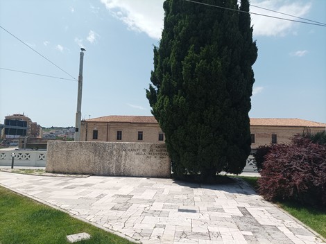 Monumento ai caduti della Resistenza immerso nel verde, con una grande conifera sullo sfondo.