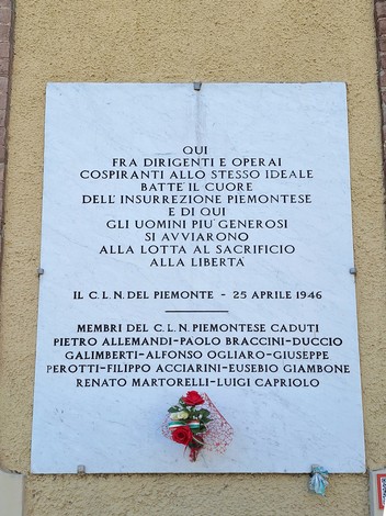Lapide commemorativa dedicata al Comitato di Liberazione Nazionale piemontese, con fiori rossi e iscrizioni storiche.