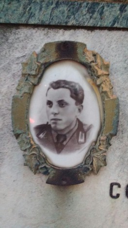 Ritratto ovale in ceramica di un giovane in uniforme, incorniciato in metallo su lapide di marmo.