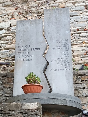 Monumento ai caduti con un obelisco in pietra e una pianta in vaso, simbolo di memoria e onore.