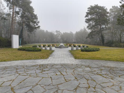 Cimitero militare italiano di Zehlendorf con un percorso centrale e lapidi in un ambiente boschivo nebbioso.