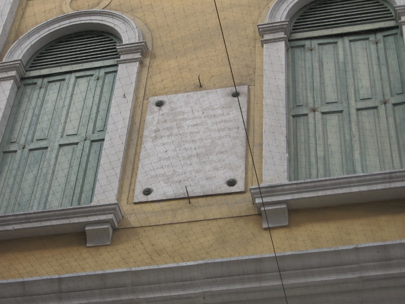 Lapide commemorativa sulla facciata del CLN di Mestre, con finestre verdi sullo sfondo.