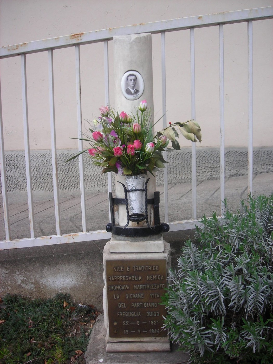 Cippo commemorativo a Freguglia, con fiori e ritratto, in onore di un martire locale.