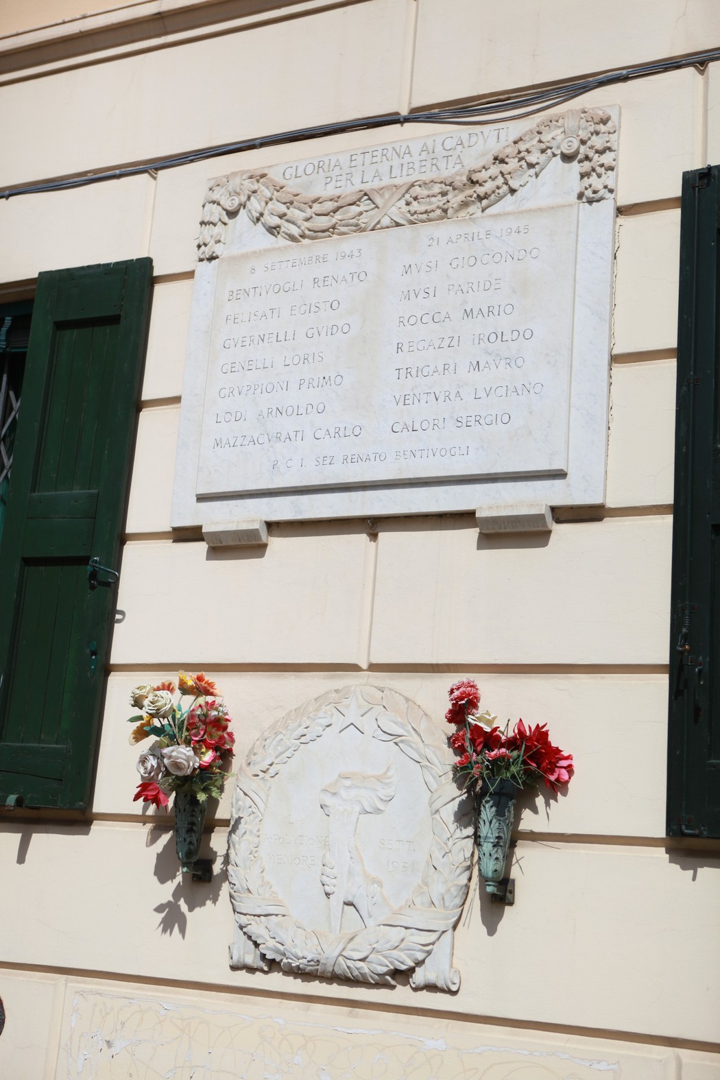 Lapide commemorativa con fiori, dedicata ai caduti per la Libertà, su un muro di un edificio.