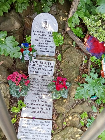 Cippo commemorativo di Enzo Fioritto, decorato con fiori, situato in un ambiente naturale.