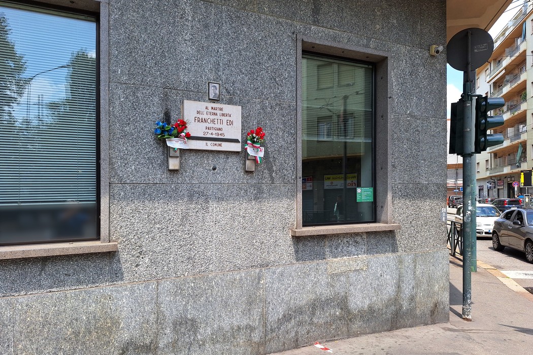 Lapide commemorativa a Franchetti, situata su una parete in granito, adornata con fiori.