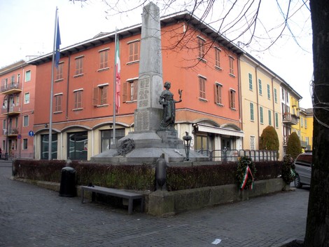 Monumento commemorativo dedicato ai caduti, situato a Pianello, circondato da edifici e piante.