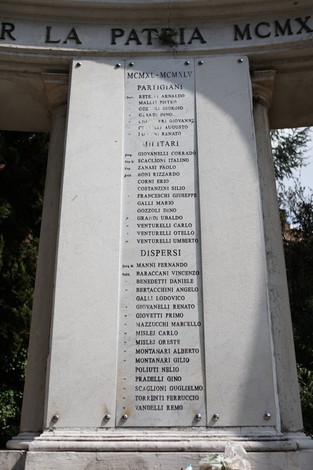 Monumento ai Caduti con nomi di partigiani e dispersi inciso su una stele, circondato da vegetazione.