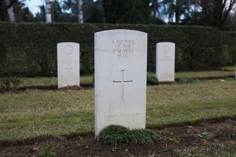 Cimitero di guerra del Commonwealth con tombe bianche e croci su un prato verde. Atmosfera di riflessione e rispetto.