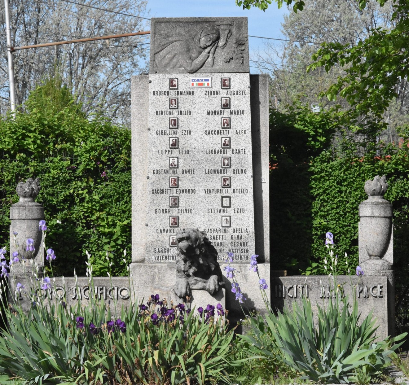 Monumento commemorativo ai caduti per la libertà di Sacca, circondato da fiori e verde.