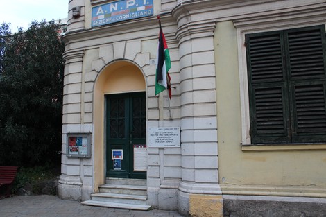 Lapide ai partigiani affissa su un edificio, con bandiere e dettagli architettonici in primo piano.