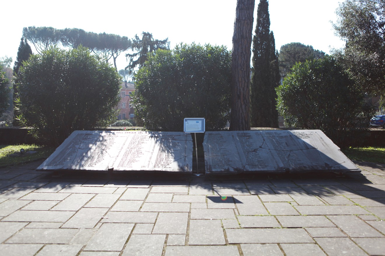 Lapidi monumentali commemorano le vittime dell'eccidio di Sant'Anna di Stazzema, circondate da verde.