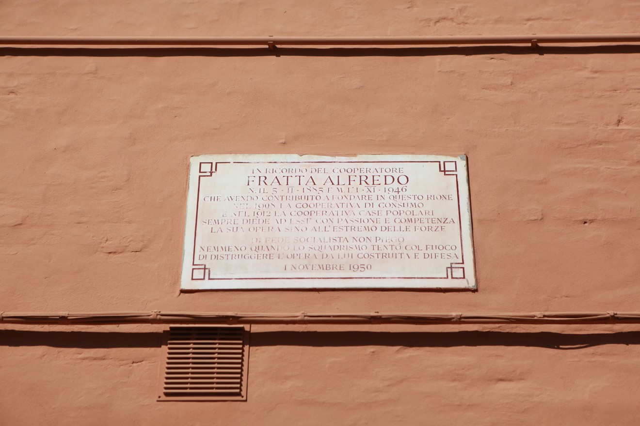 Lapide commemorativa a Fratta, dedicata a un contributore importante, situata su una parete color chiaro.