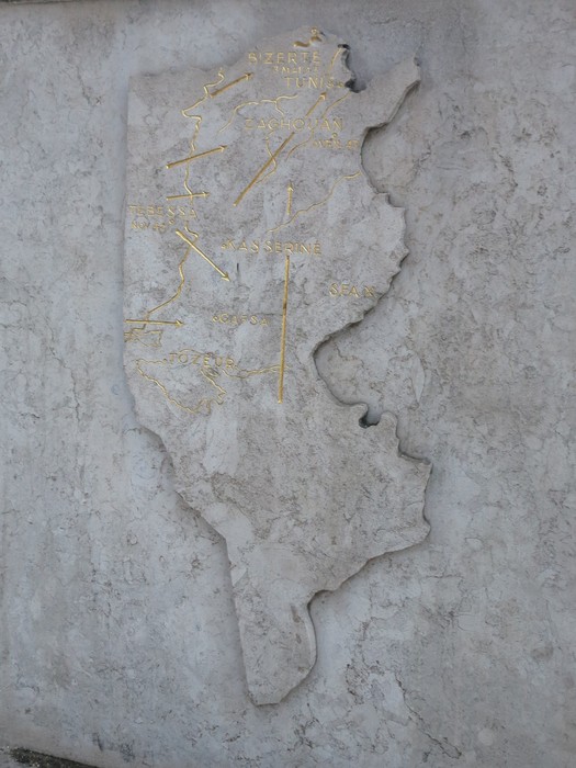Statua in pietra che rappresenta una mappa stilizzata, con dettagli dorati su fondo chiaro.