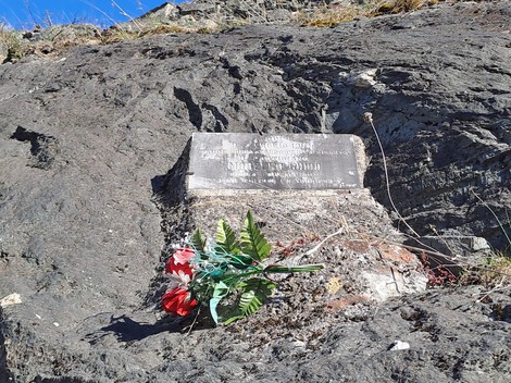 Lapide commemorativa dedicata a Morello, posizionata su un terreno roccioso con fiori decorativi.