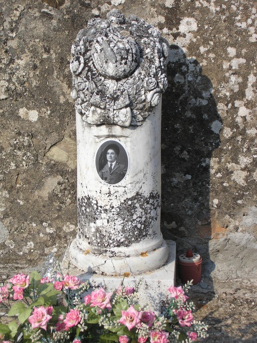 Sepolcro di Santini con colonna decorativa e fotografia commemorativa. Fiori colorati adornano il luogo.