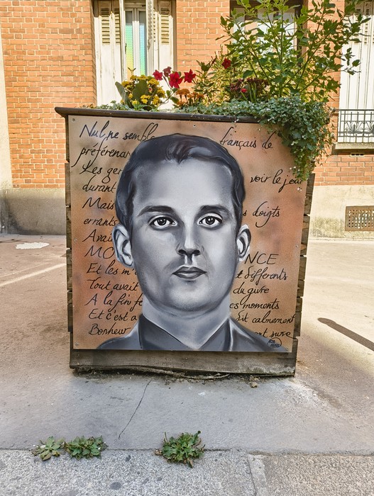 Ritratto commemorativo di un membro del Gruppo Manouchian su un cassonetto decorato con scritte evocative.