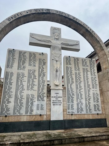 Monumento commemorativo con croce e pannelli in marmo riportanti nomi di caduti. Atmosfera di rispetto e memoria.