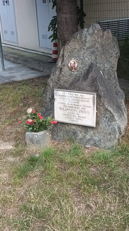Cippo commemorativo a Mulassano, con una fotografia e una base in pietra circondato da fiori.