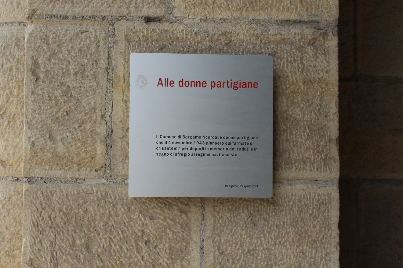 Targa commemorativa dedicata alle donne partigiane, situata su un muro di pietra a Bergamo.