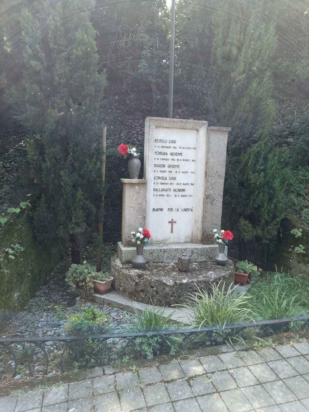 Monumento ai cinque martiri, circondato da alberi e fiori, simbolo di memoria e onore.