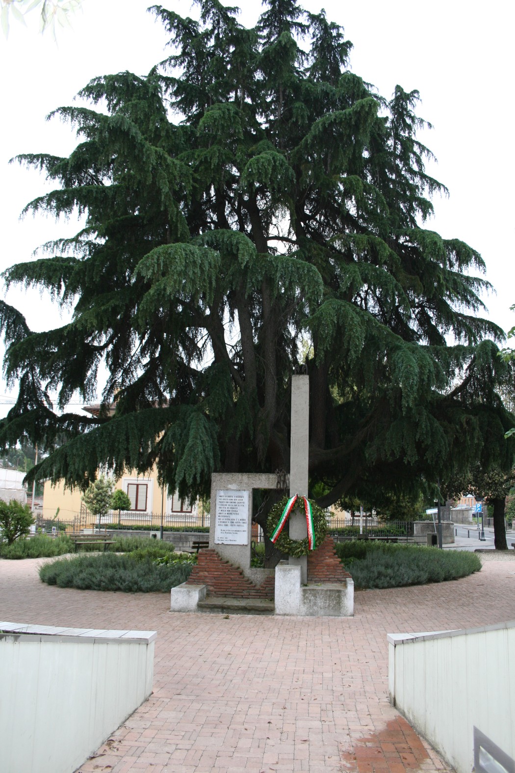Monumento del ventennale, circondato da alberi e piante, punto di riferimento commemorativo in un contesto urbano.