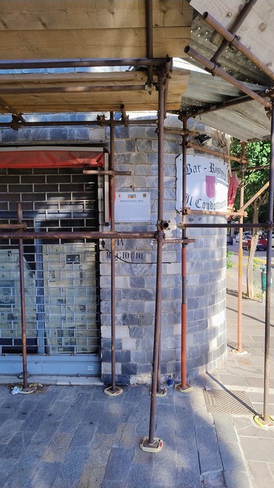 Targa di un bar con impalcatura in primo piano, situata in un'area urbana.