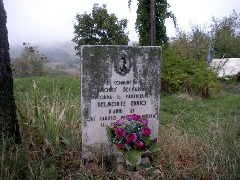Lapide commemorativa dedicata al partigiano Delmonte Emnio, situata in un paesaggio rurale.