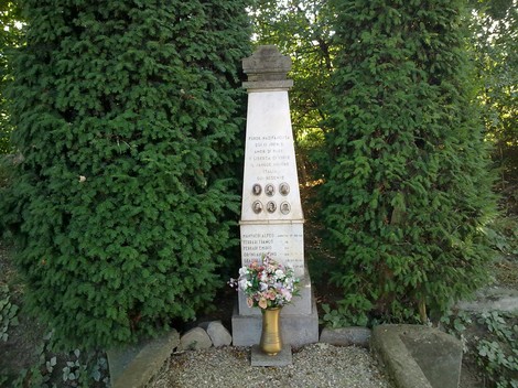 Monumento commemorativo a Manfredi e altri, circondato da alberi e decorato con fiori.