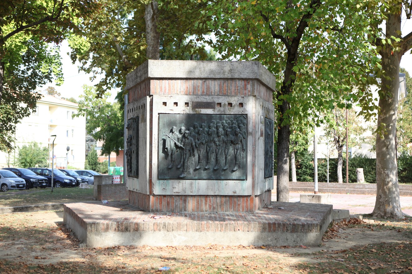 Monumento alla Resistenza, circondato da alberi, con pannelli commemorativi e un'area verde circostante.