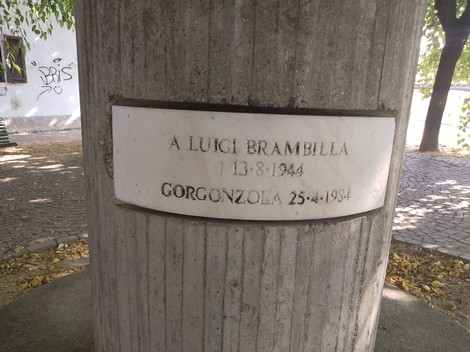 Monumento a Brambilla con una dedica intitolata a Luigi Brambilla, situato in un contesto verde e urbano.