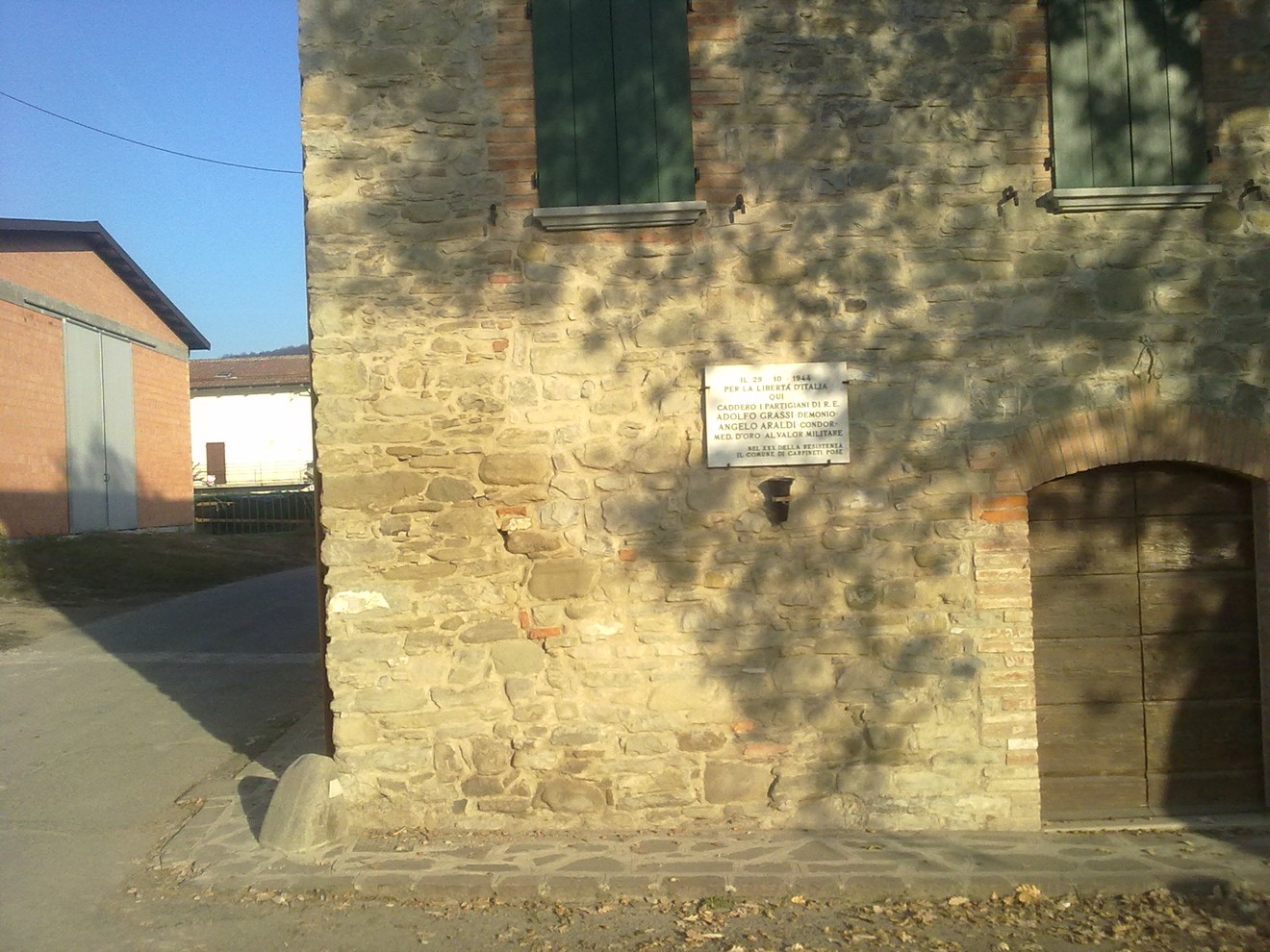 Lapide commemorativa su una parete di pietra, in un contesto rurale tranquillo e suggestivo.