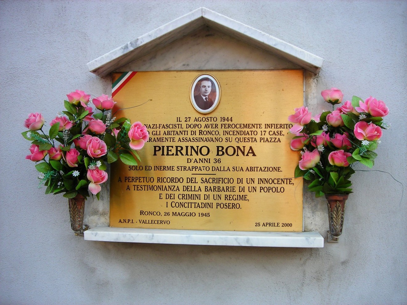Targa commemorativa in memoria di Pierino Bona, vittima del nazifascismo a Ronco, con fiori decorativi.
