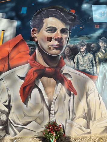 Murale a Frosinone che ritrae un giovane con un fazzoletto rosso, sullo sfondo scene di vita quotidiana.